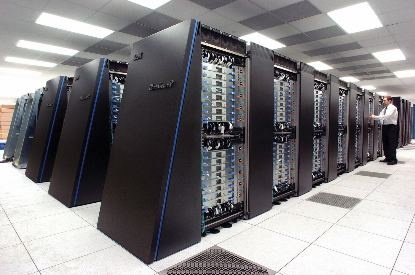 Rows of supercomputer cabinets in a large hall with a person at the end